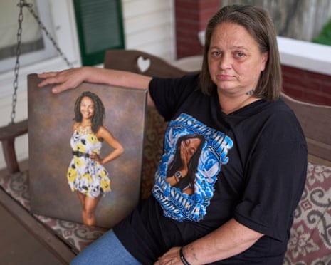Woman in black T-shirt with picture of daughter sits on porch swing with arm resting on picture of smiling young woman in dress.