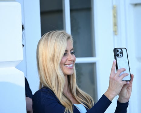 A blond woman smiles as she holds up her iPhone to take a picture