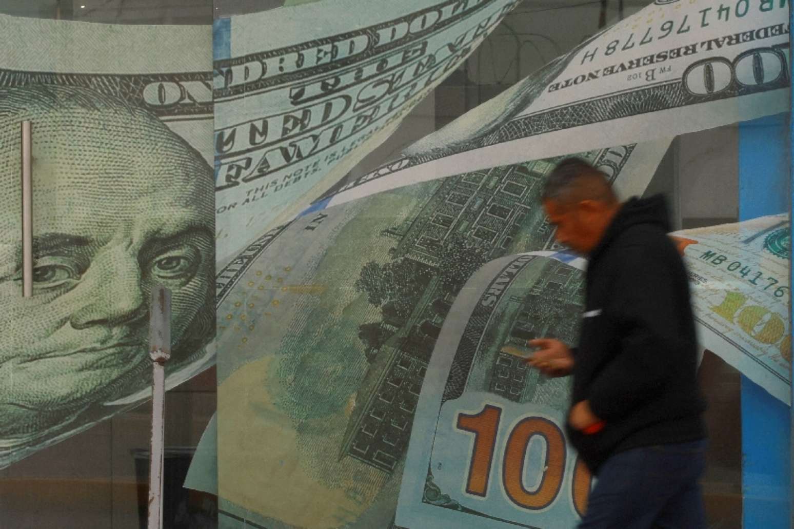 Um homem passa em frente a uma casa de c&acirc;mbio, com adesivos de notas de d&oacute;lar na porta e nas paredes