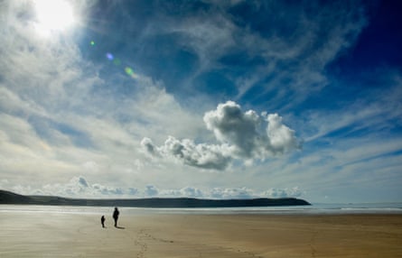A large yellow sand beach with only two people walking on it with a bright blue sky and white clouds above